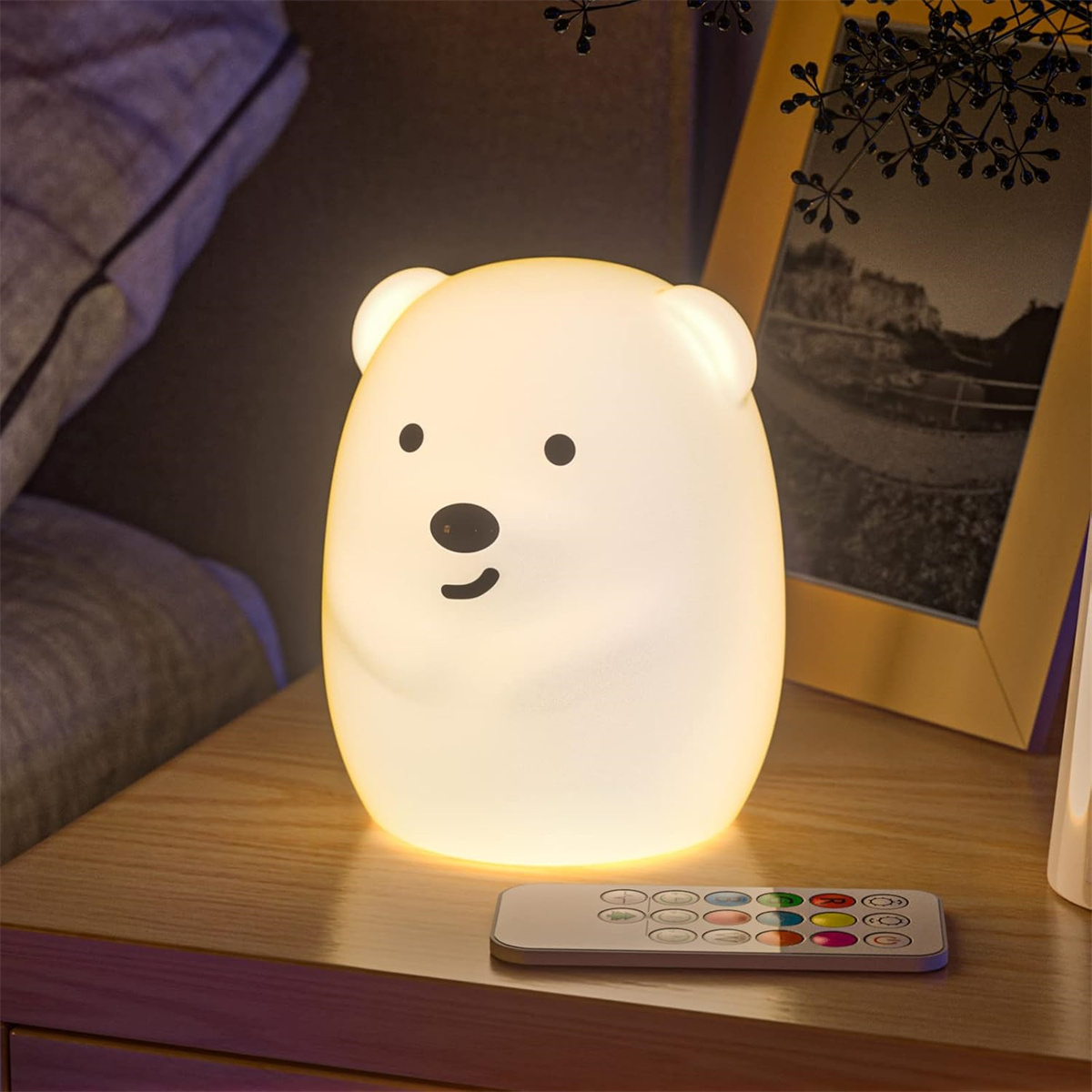 Ein weißes bärenförmiges Nachtlicht mit Fernbedienung. Das Licht steht auf einem Holztisch.