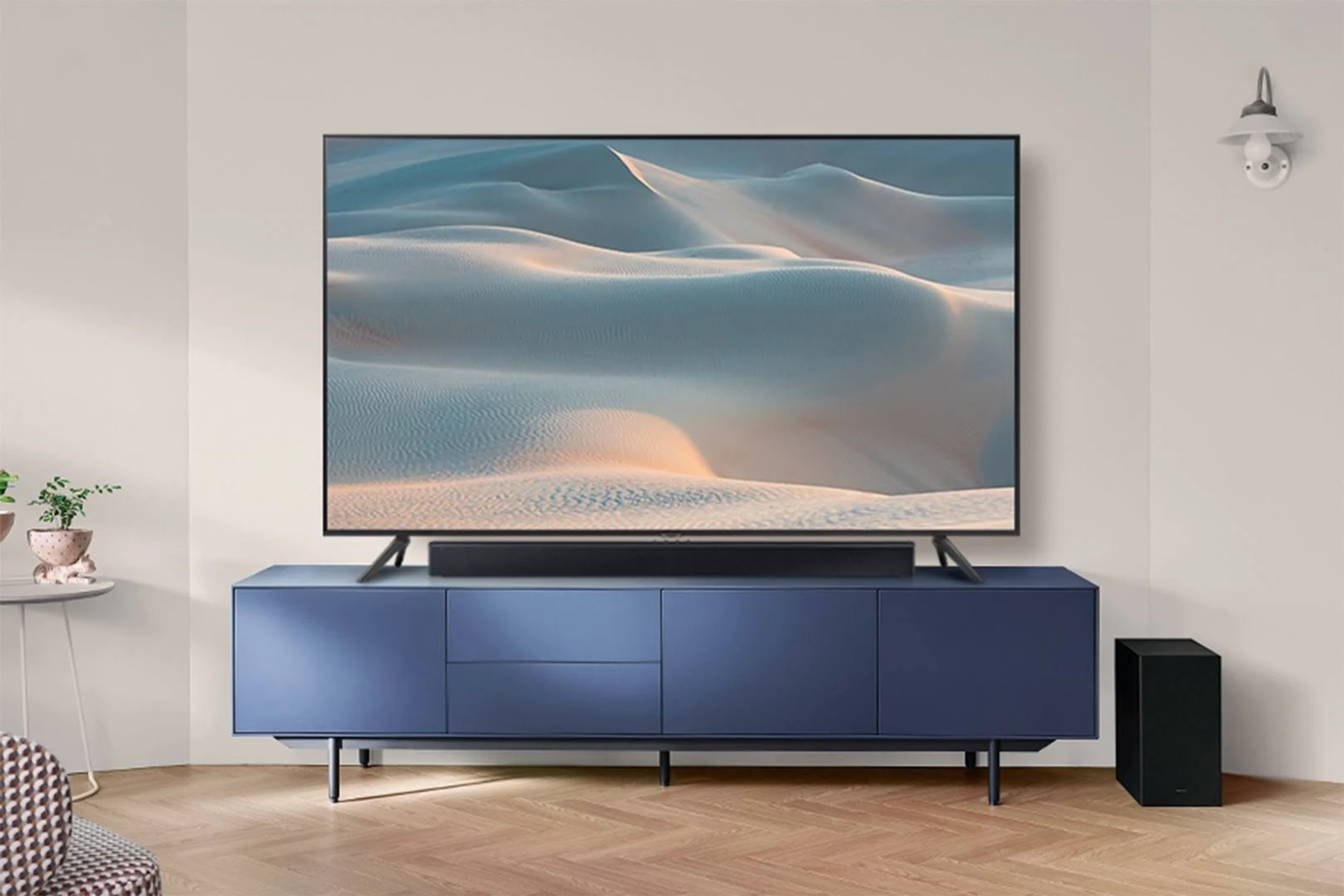 Escena de sala de estar con un televisor grande sobre un mueble azul, barra de sonido y un subwoofer negro.