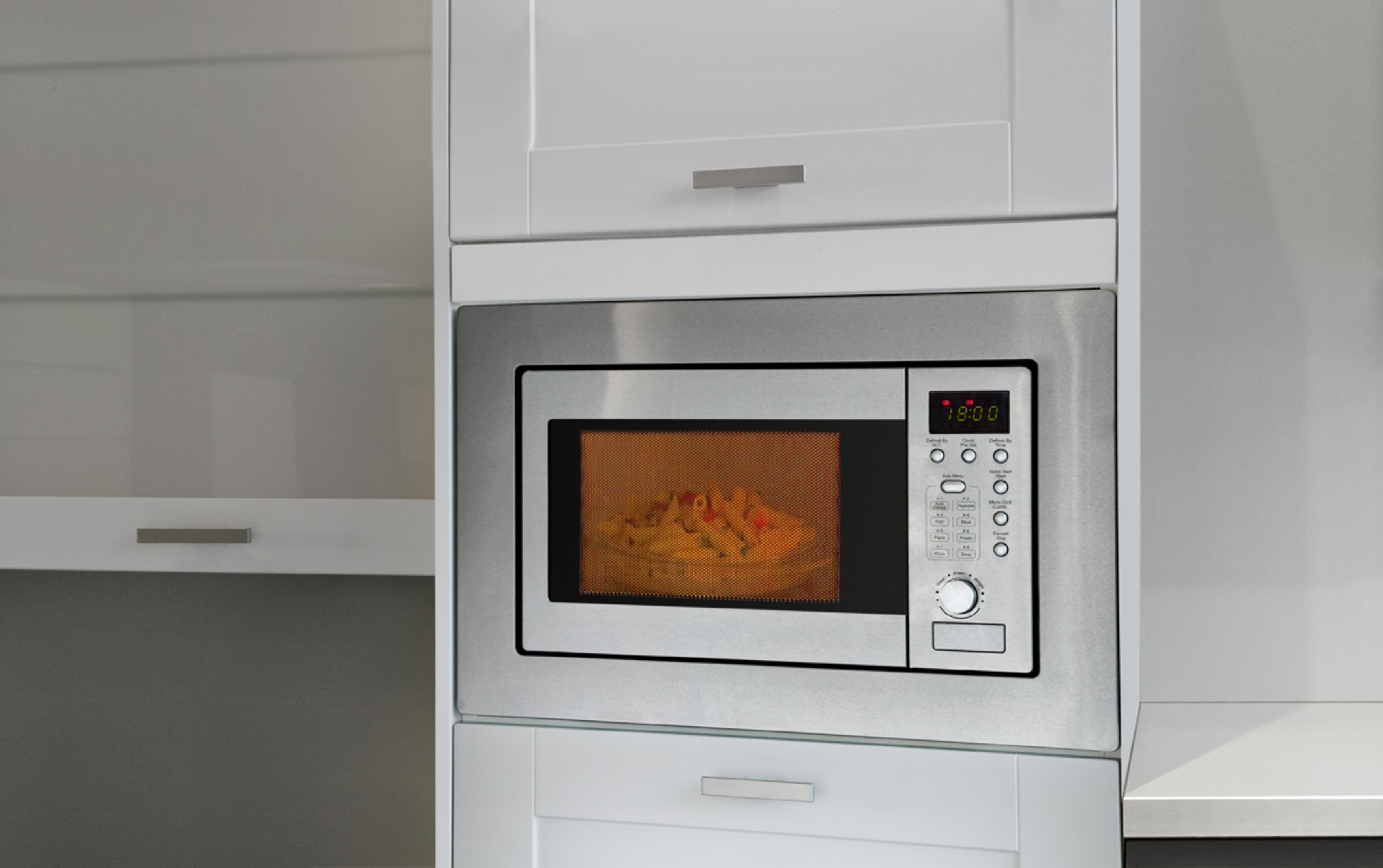 Mikrofalówka w szafce. Ma jedzenie w środku. Drzwi szafki są białe.