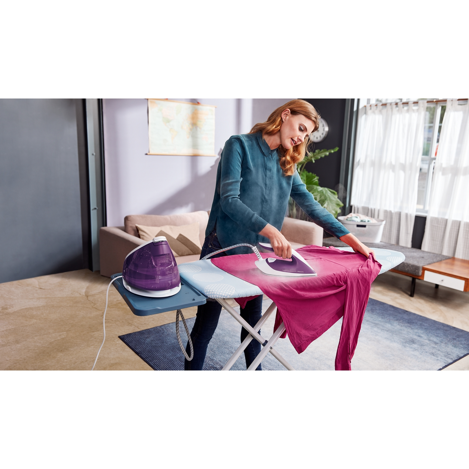 Kobieta prasująca różową koszulę na niebieskiej desce do prasowania, biały generator pary w tle.