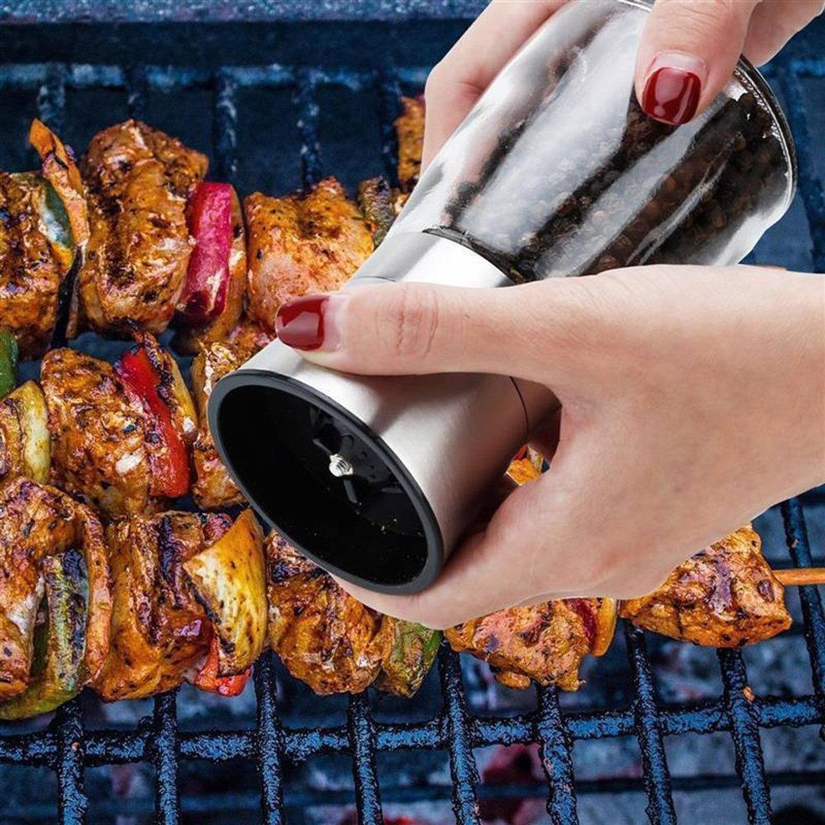 Hände, die eine Pfeffermühle über einem Grill mit Grillgut benutzen.