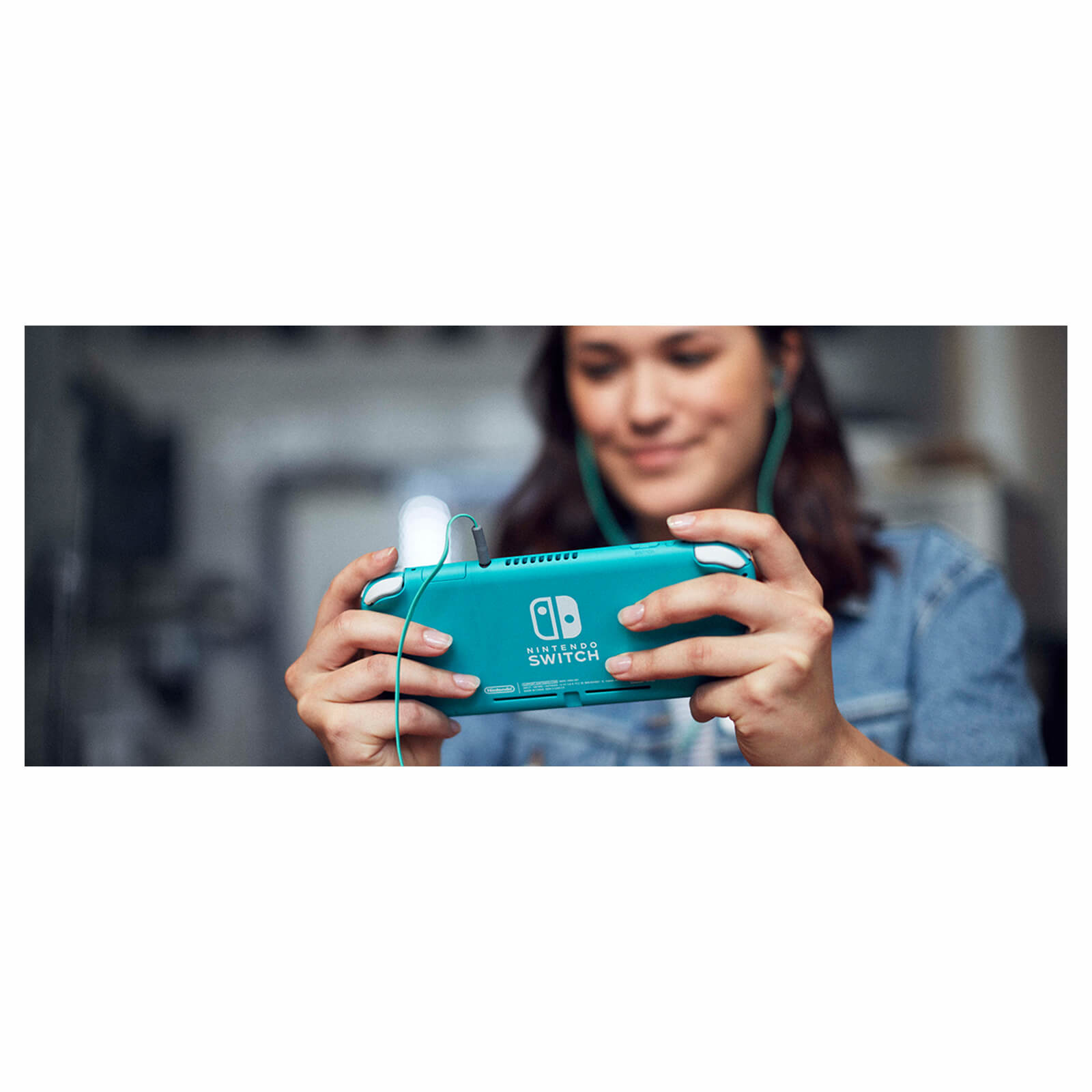 Eine Frau hält eine türkisfarbene Nintendo Switch-Konsole. Sie trägt ein Jeanshemd und hat grüne Kopfhörer.