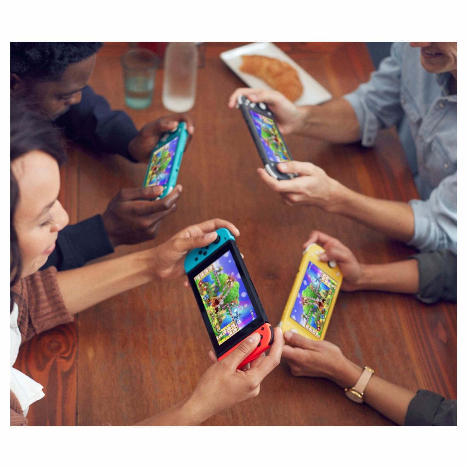 Vier Personen sitzen um einen Tisch und spielen Videospiele auf Handheld-Konsolen.