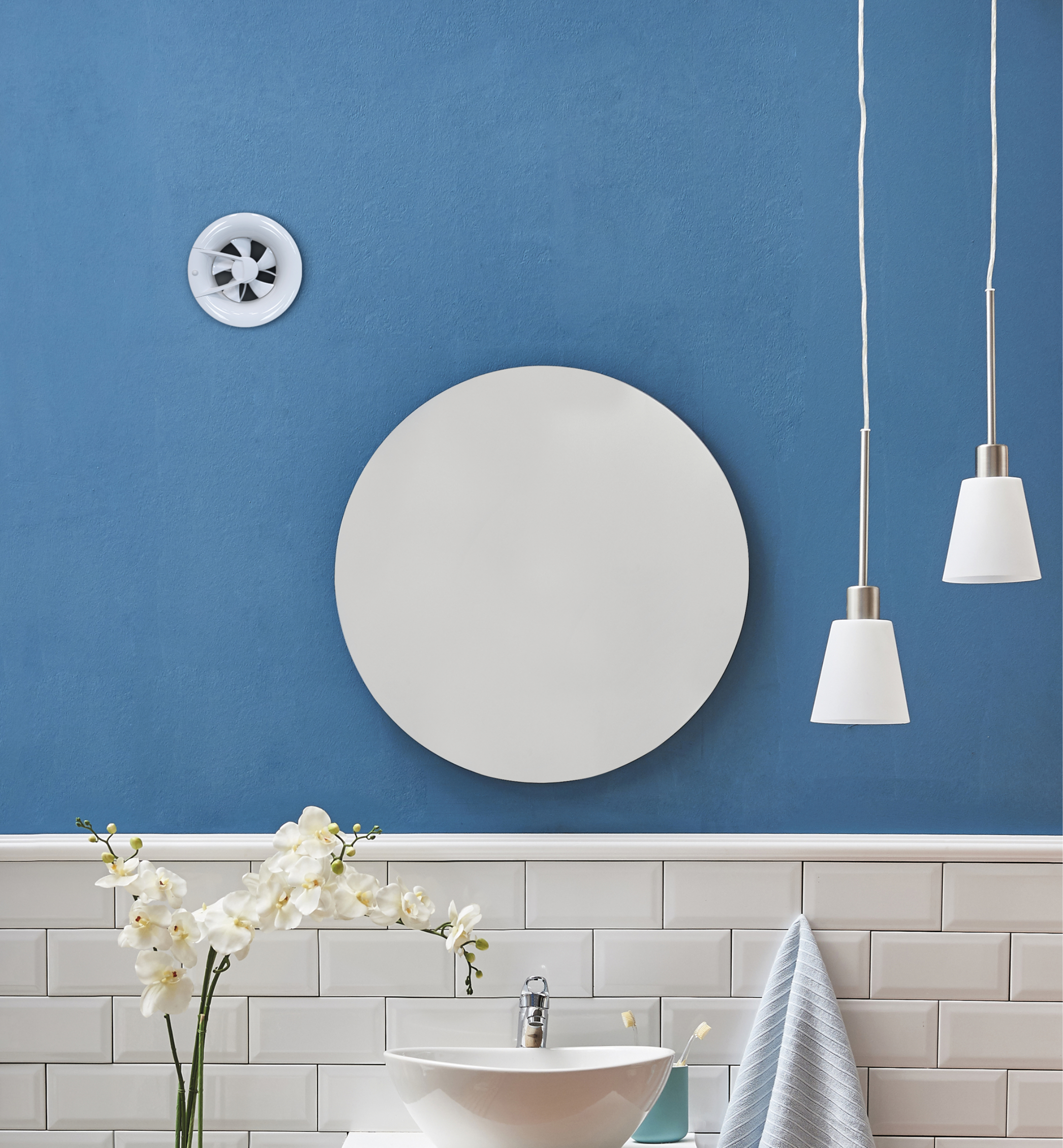 Ein Badezimmer mit weißem Waschbecken, Spiegel, Wandlüfter und Hängelampen vor einer blauen Wand.