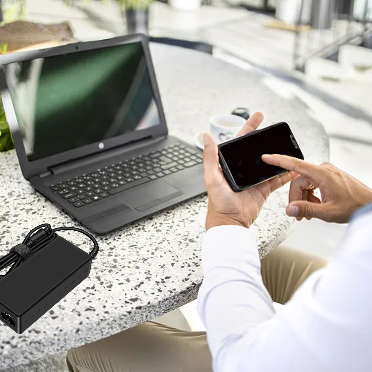 Person nutzt Smartphone neben Laptop und Netzteil.