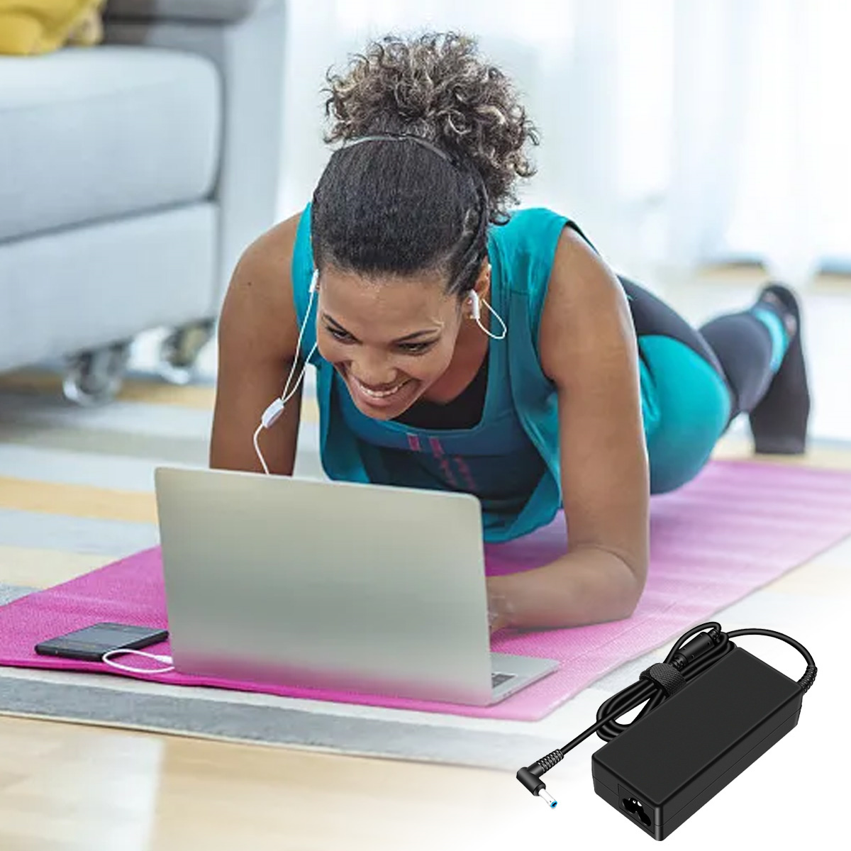 Frau auf Yogamatte, die einen Laptop mit Kopfhörern, ein Telefon und ein schwarzes Netzteil benutzt.