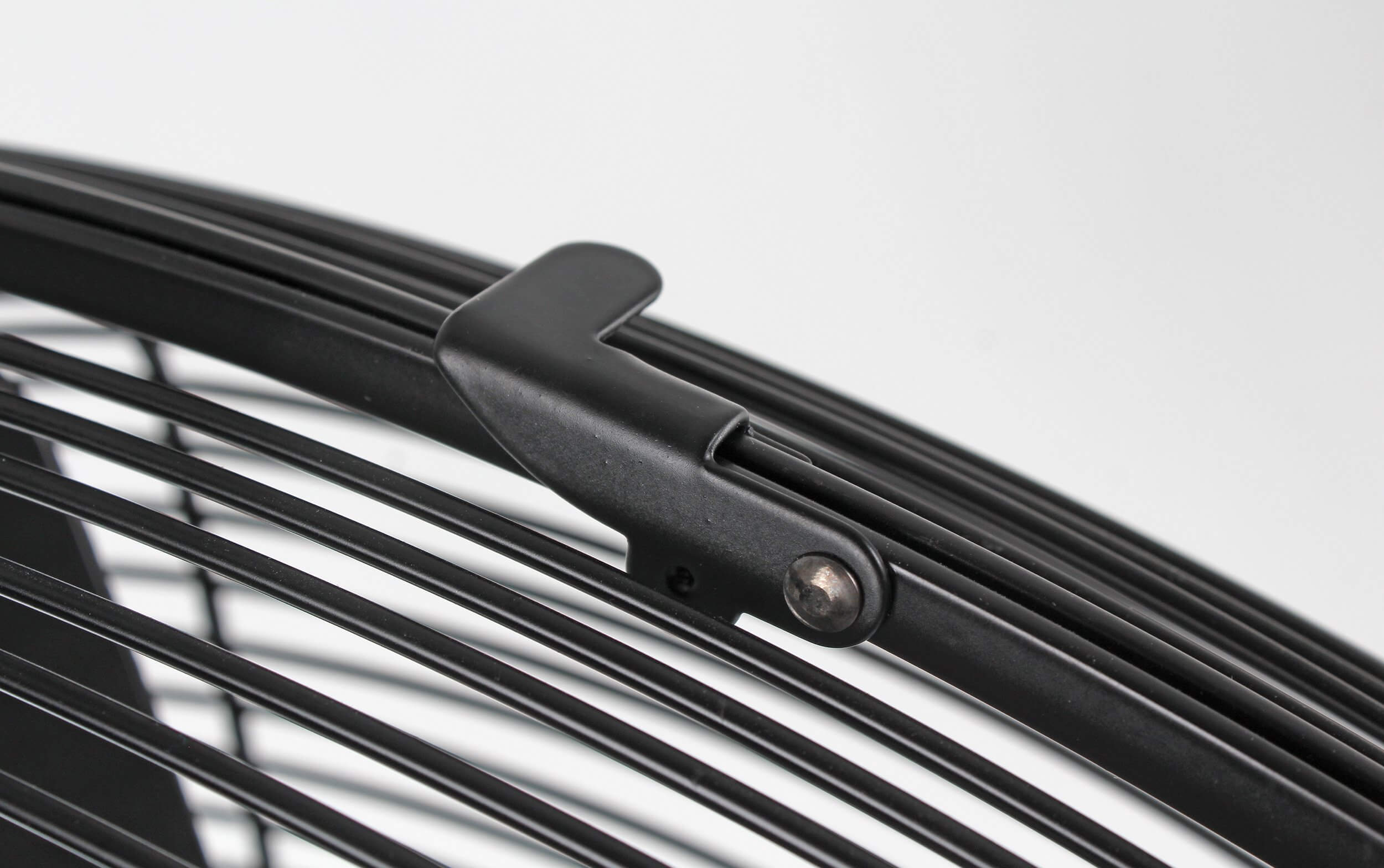 Nahaufnahme des Schutzgitters eines schwarzen Ventilators und eines schwarzen Clips. Das Gitter hat horizontale Stäbe.