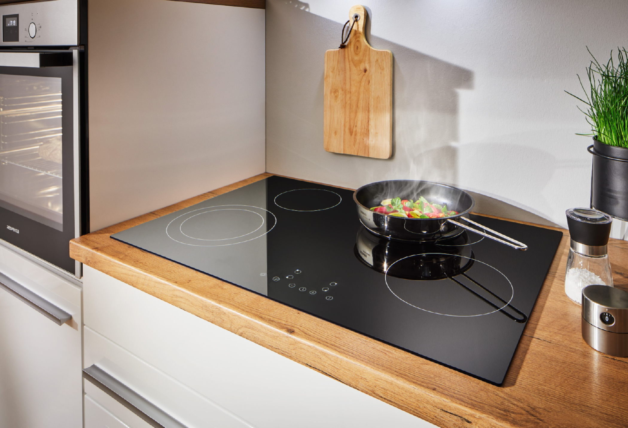 Scena di cucina. Un piano cottura con padella di cibo, tagliere e forno sullo sfondo.