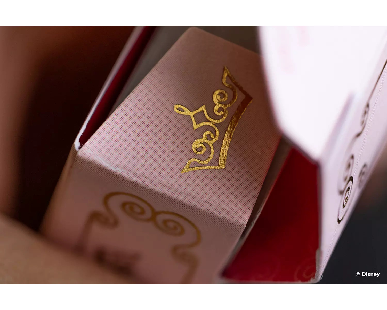Rosa und goldene Spielkartenbox mit Kronen-Design. Disney-Logo unten.