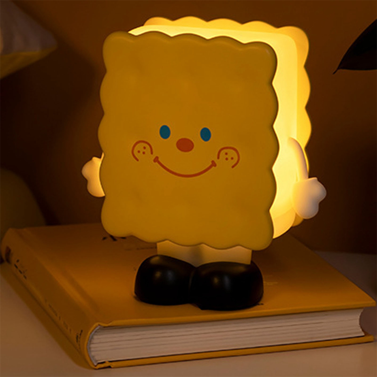 Gelbe Cartoon-Charakter-Lampe mit einem lächelnden Gesicht auf einem gelben Buch.