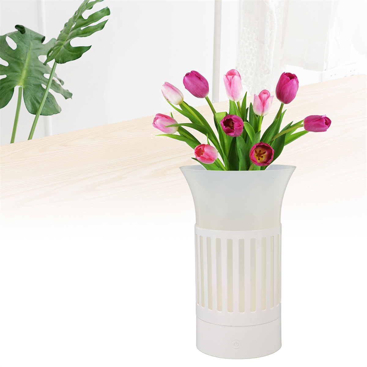 Weiße Vase mit Tulpen. Grüne Blätter im Hintergrund, heller Holztisch.