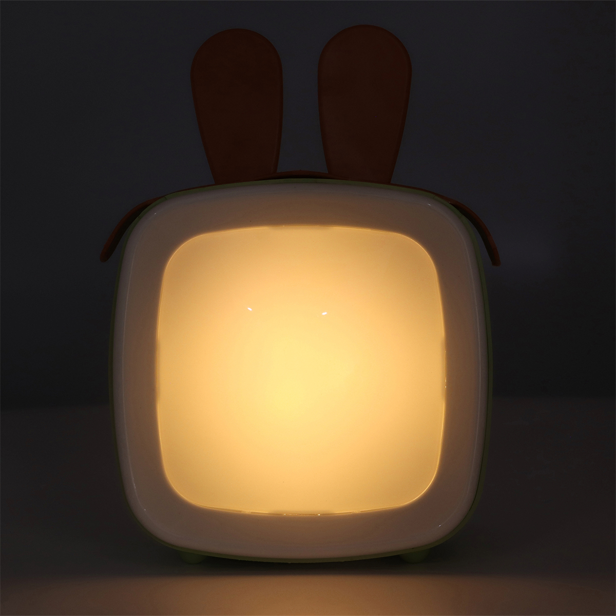 Niedliche Nachtlampe in Form eines Fernsehers mit Hasenohren. Sie leuchtet sanft gelb in einem dunklen Raum.