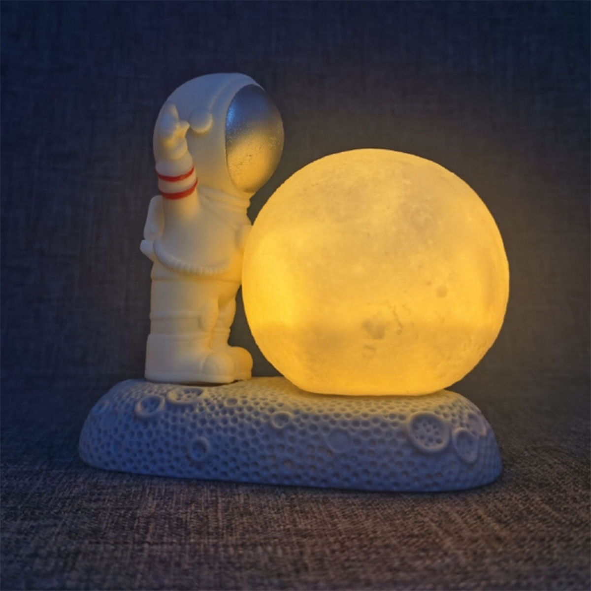 Eine weiße Astronautenfigur steht neben einer gelben Mondlampe auf weißer Basis mit Kratern.