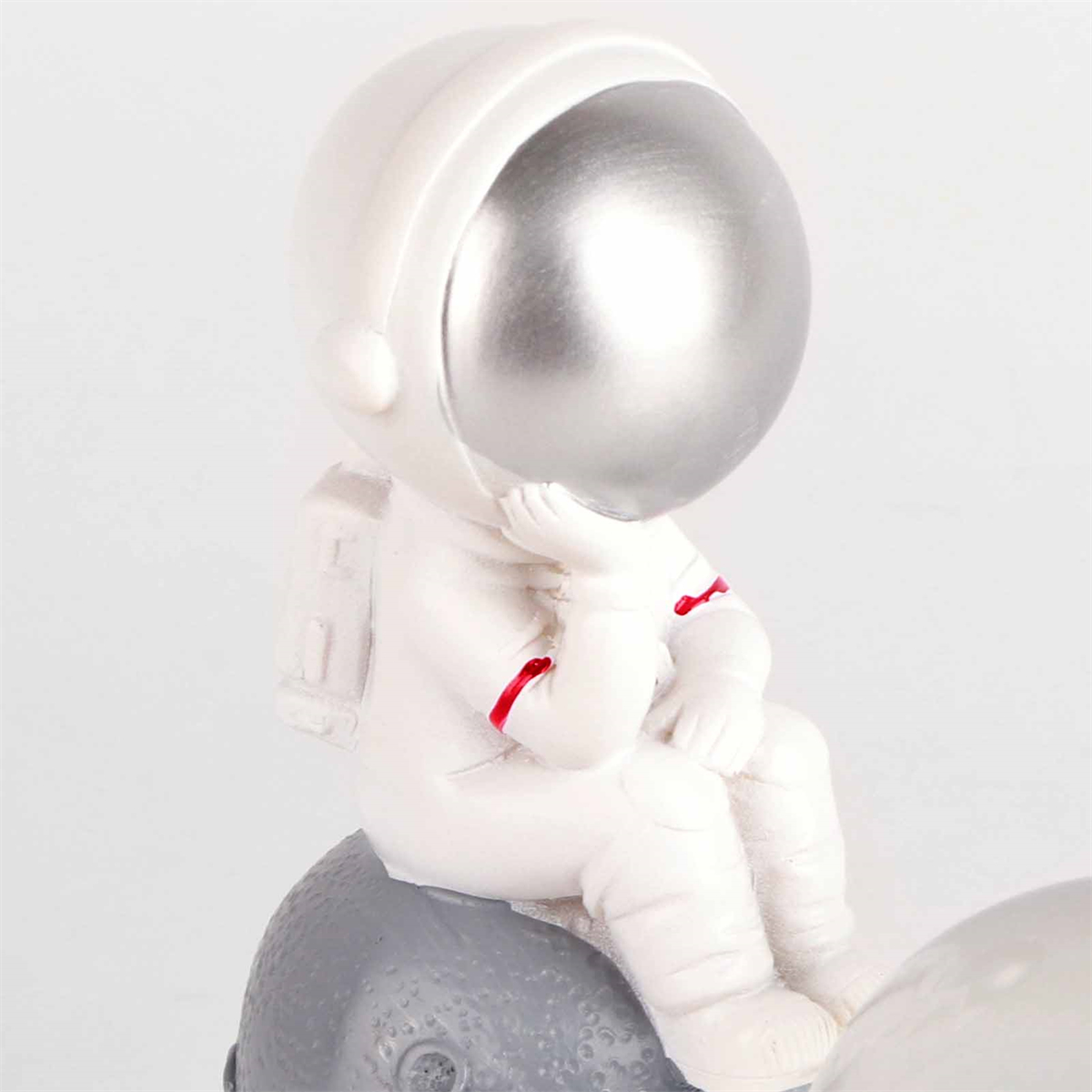 Eine Figur eines Astronauten, der auf einem Mond sitzt. Der Astronaut trägt einen weißen Raumanzug.