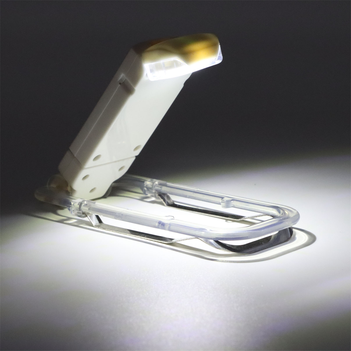 Weiße und transparente faltbare Buchlampe, abgewinkelt. Das Licht ist an.