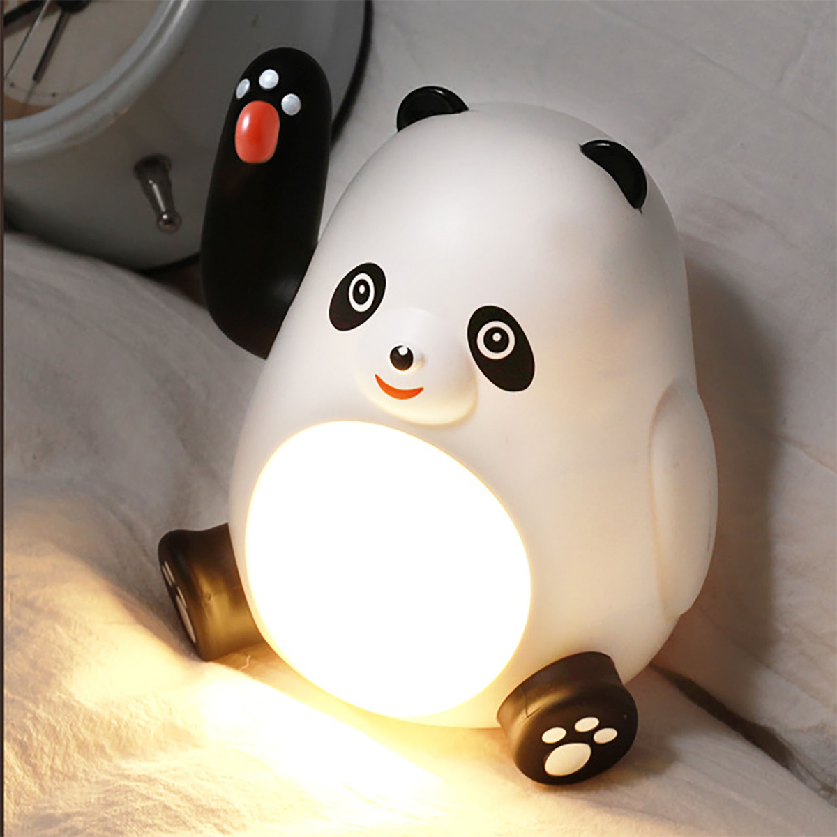 Eine panda-förmige Lampe, aus deren Körper Licht kommt. Die Lampe steht auf einem Bett.