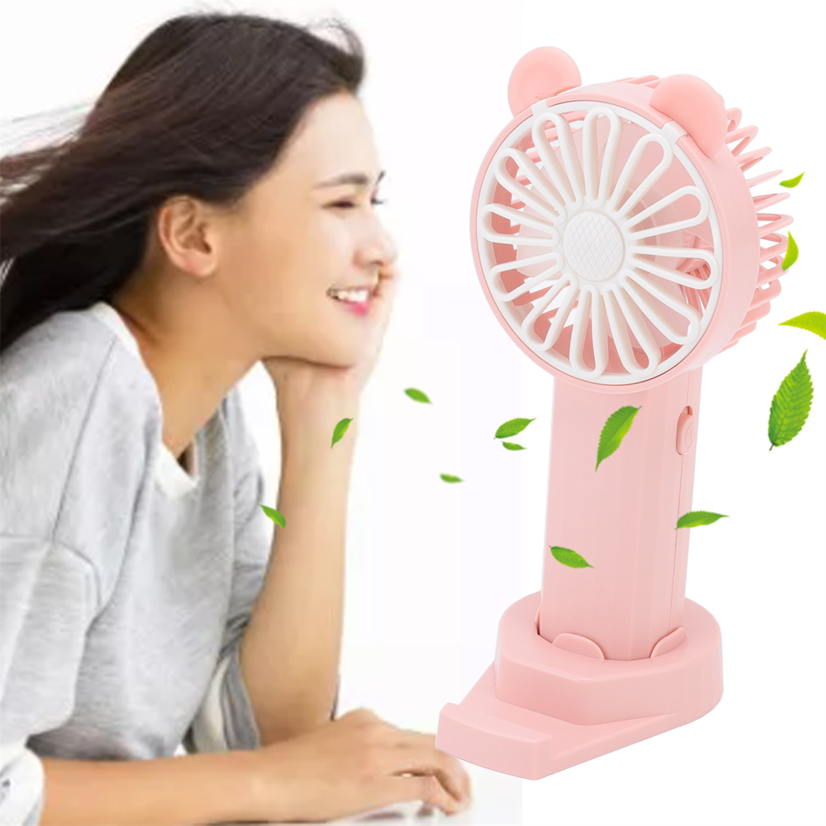 Pinkfarbener Mini-Ventilator mit Bärenohren, der einer Frau Luft zufächelt. Grüne Blätter sichtbar.