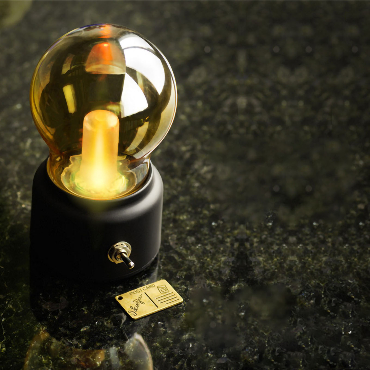 Schwarze und goldene Lampe mit einer Vintage-Glühbirne. Eine kleine goldene Postkarte daneben.