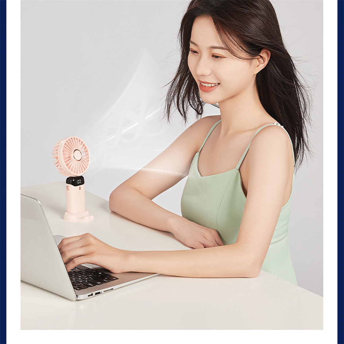Frau benutzt Laptop mit kleinem rosa Ventilator. Sie trägt ein grünes Kleid.