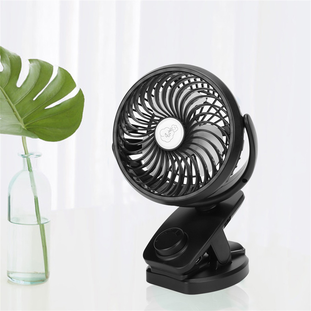Ein schwarzer Clip-Ventilator mit drehbarem Käfig. Der Ventilator steht auf einer weißen Oberfläche.