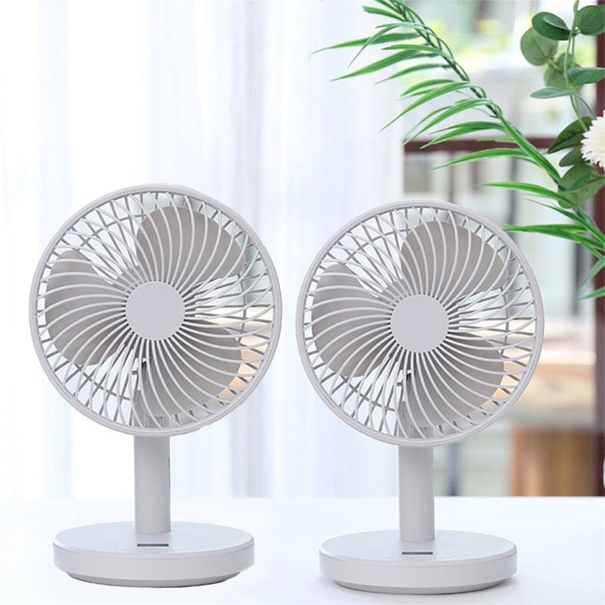 Zwei kleine weiße Ventilatoren auf Ständern mit gebogenen Flügeln, auf weißer Oberfläche.