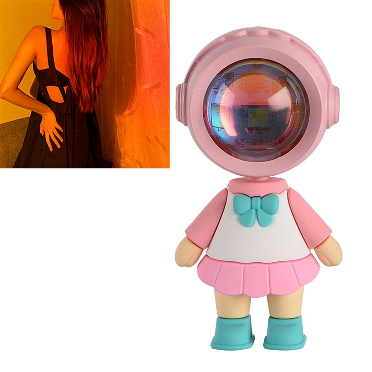 Rosa puppenförmiger Projektor mit einem projizierten Mädchenbild. Auf der linken Seite ist eine Frau in einem schwarzen Kleid zu sehen.