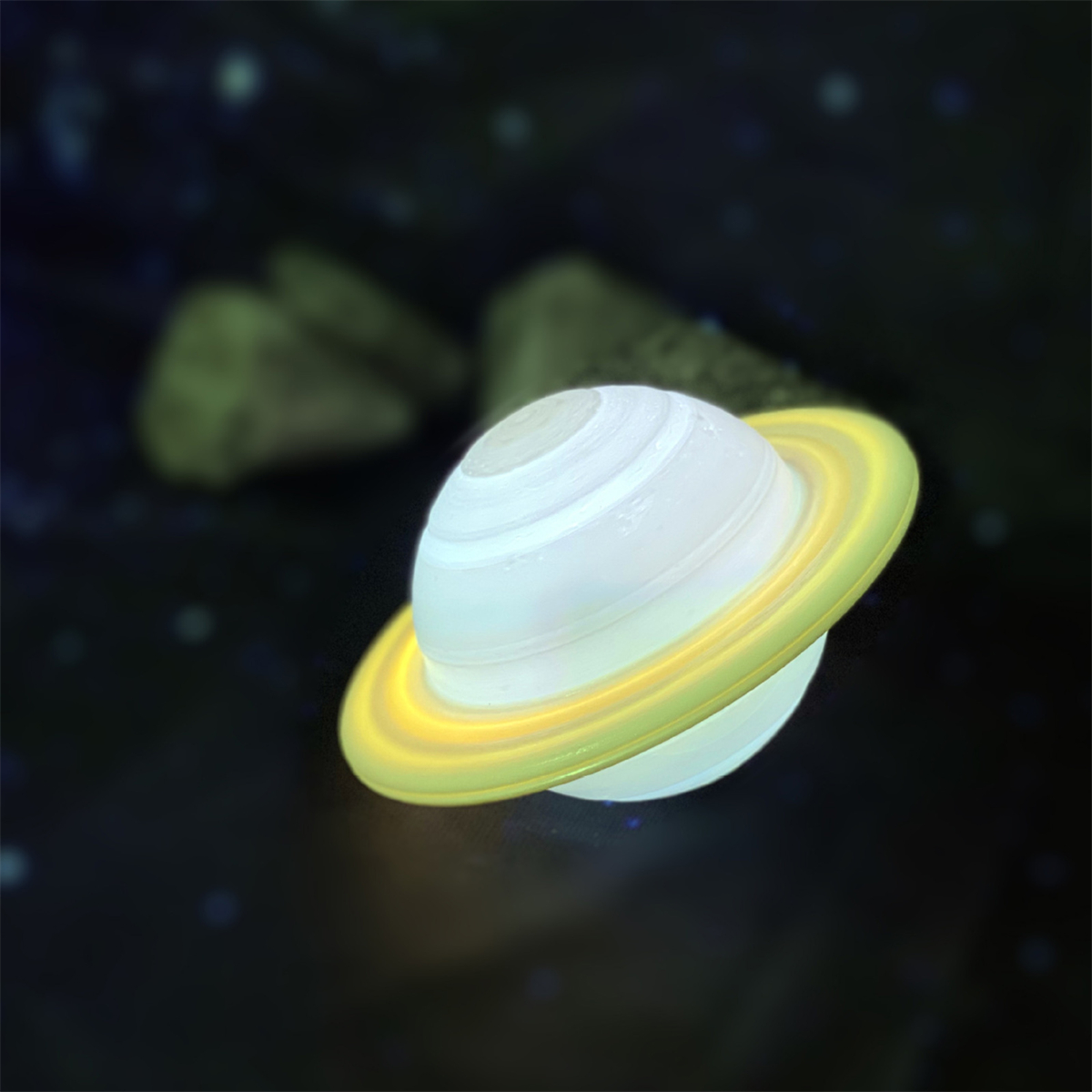 Eine leuchtende Saturnlampe mit Ringen, vor dunklem, sternenübersätem Hintergrund.