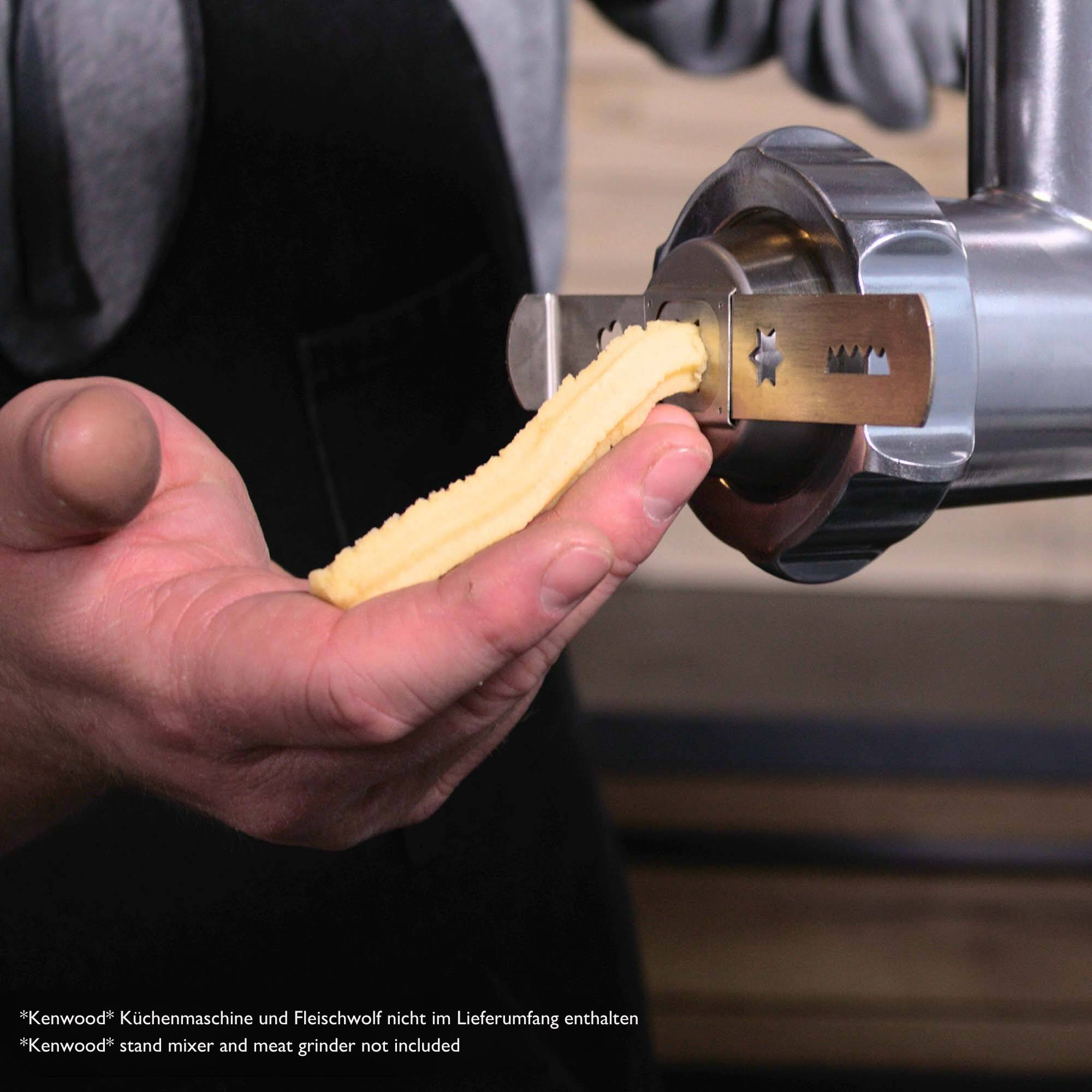 Hände einer Person, die ein Stück verarbeitetes Essen halten, das aus einem Fleischwolf extrudiert wird.