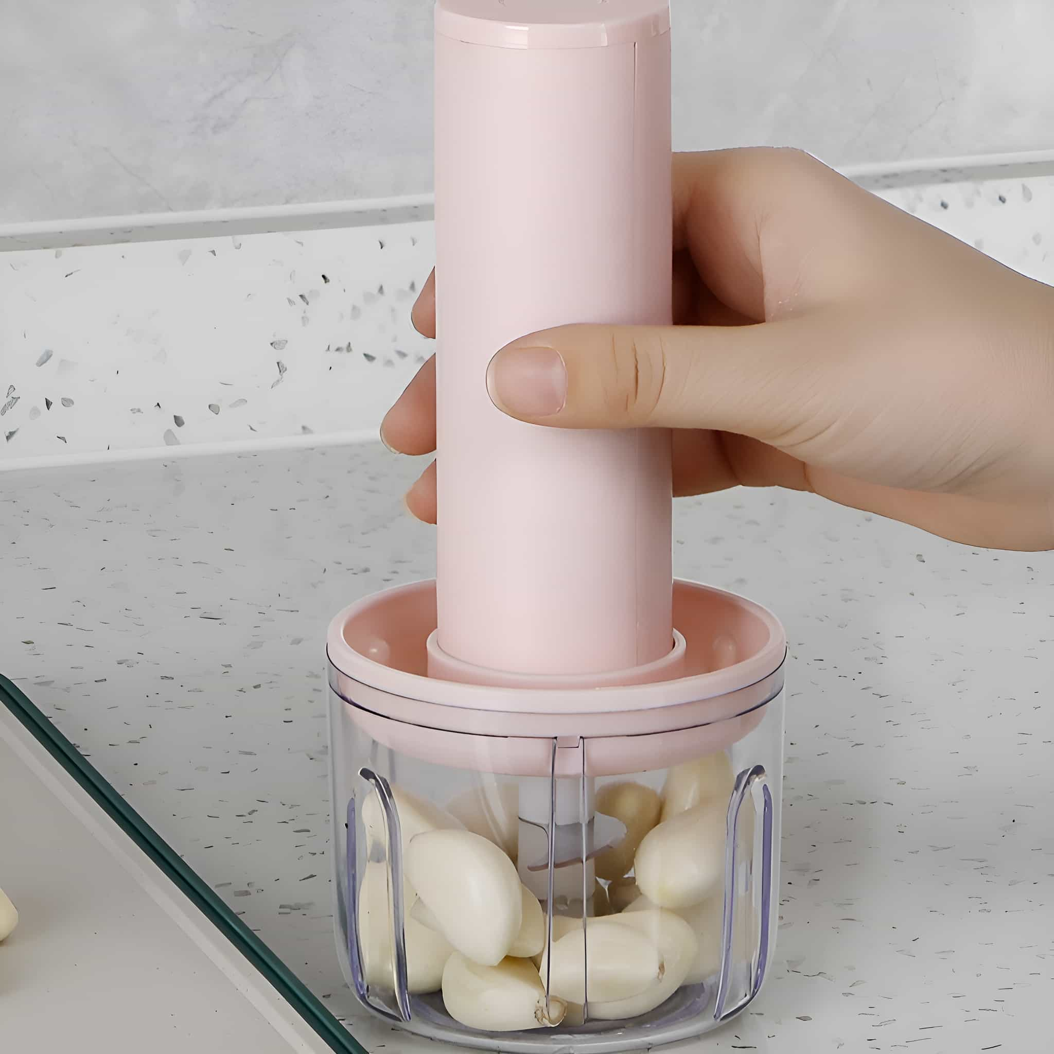 Ein rosa und klarer Knoblauchzerkleinerer mit Knoblauchzehen im Inneren, auf einer hellen Arbeitsplatte.