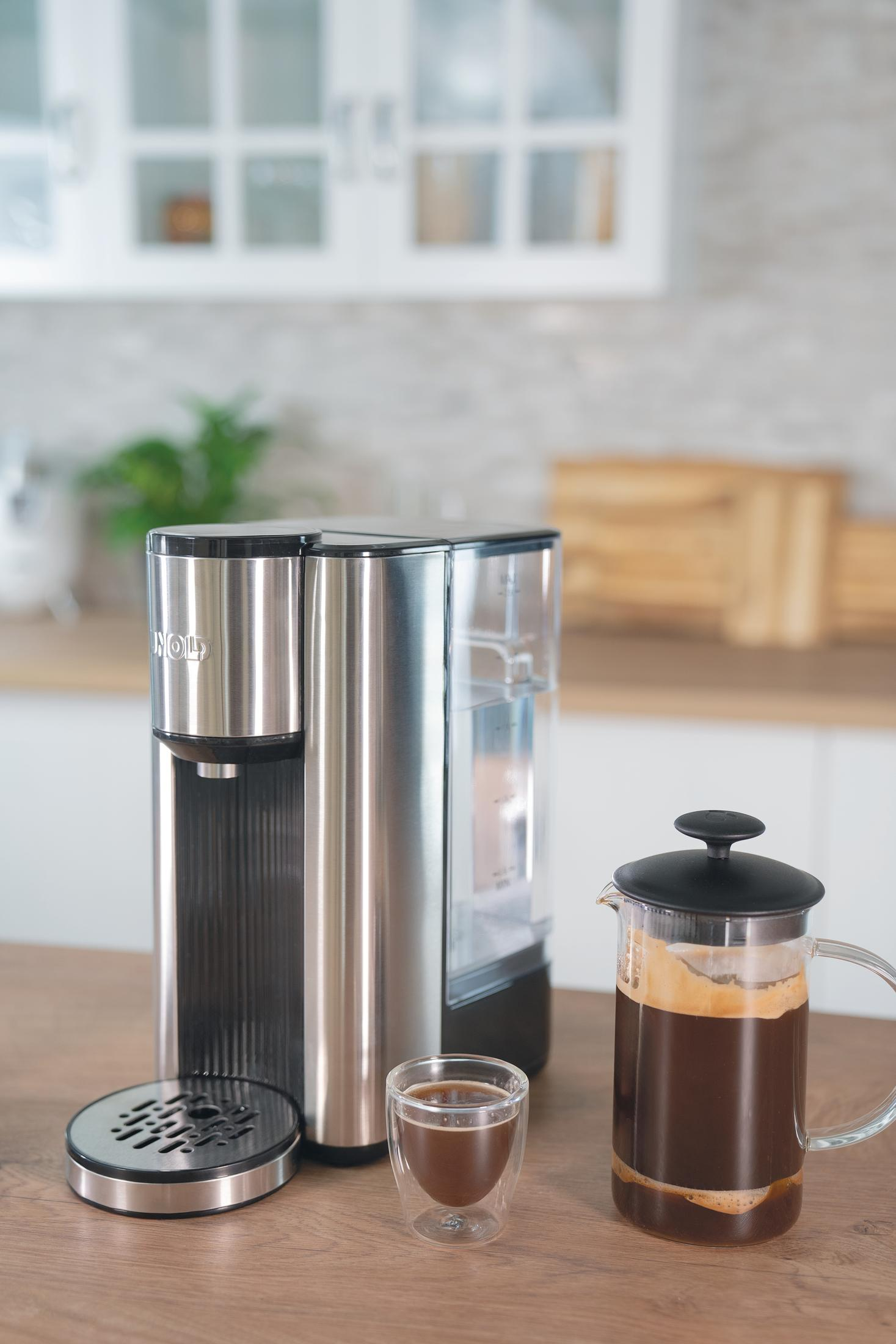 Kaffeemaschine, Glaskaraffe und ein Glas mit Kaffee auf einer Holzoberfläche in einer Küche.