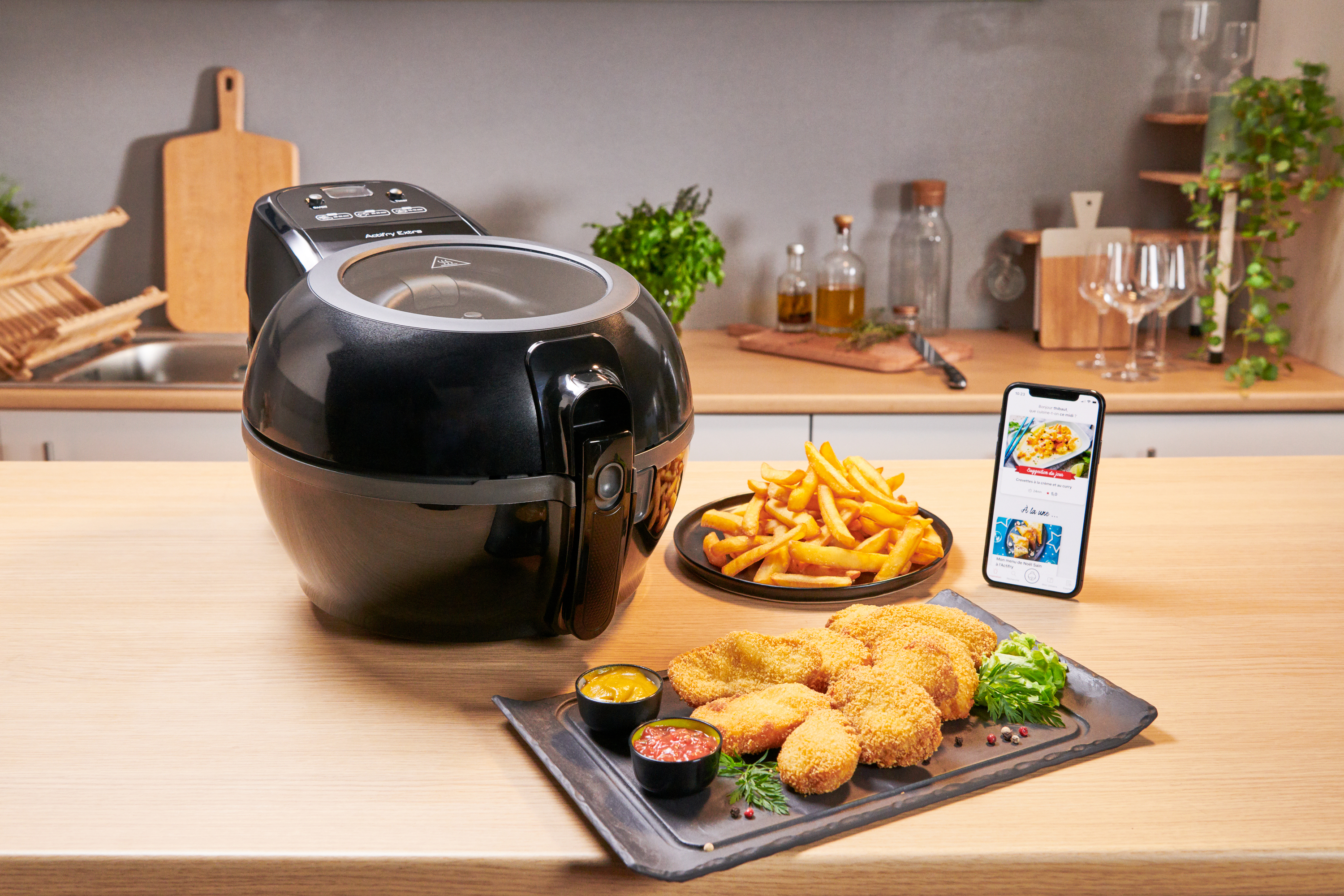 Freidora de aire con comida en mesa y móvil con receta. Fondo de cocina.