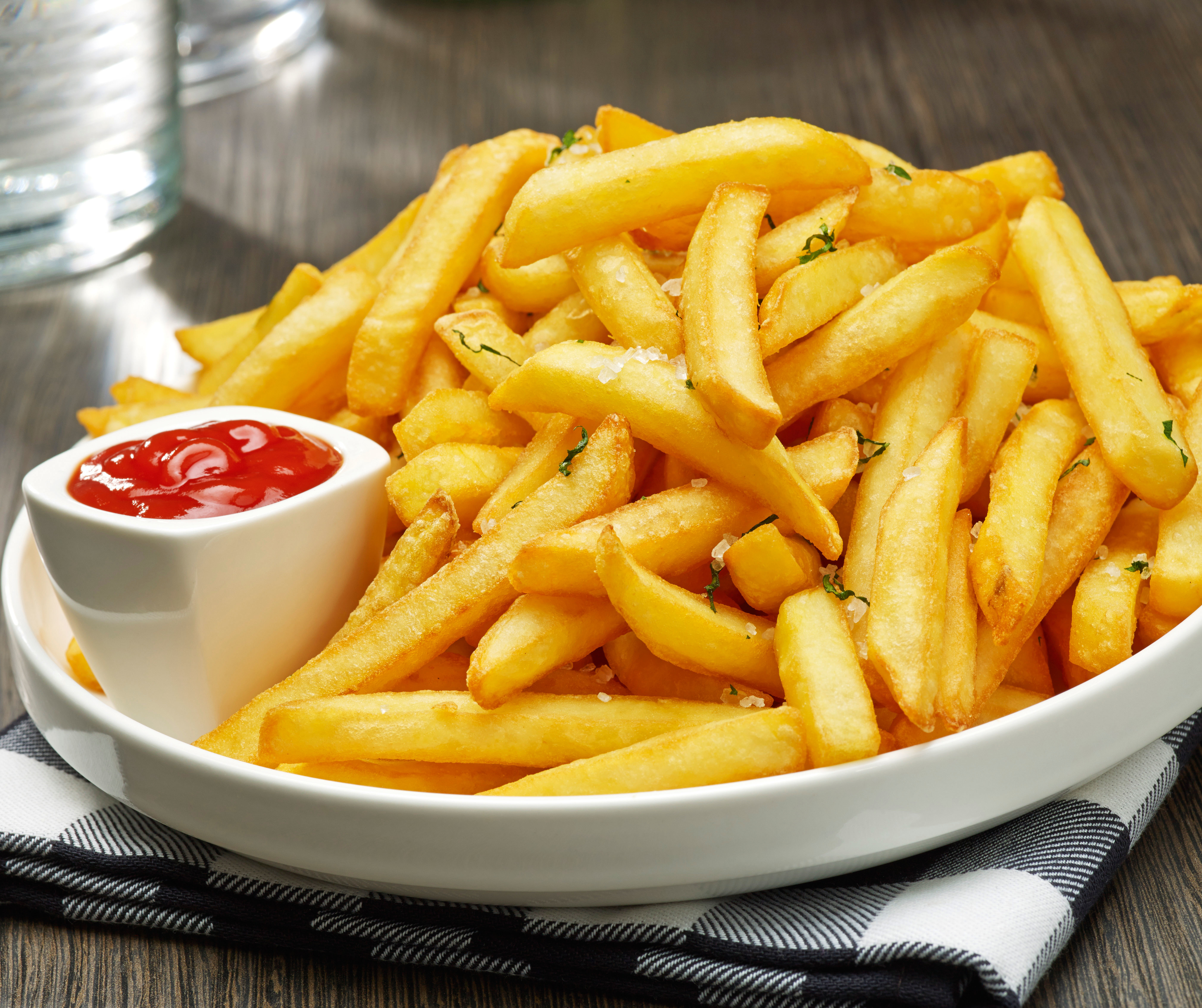 Miska złotych frytek z małą miseczką ketchupu i szmatką w kratę.