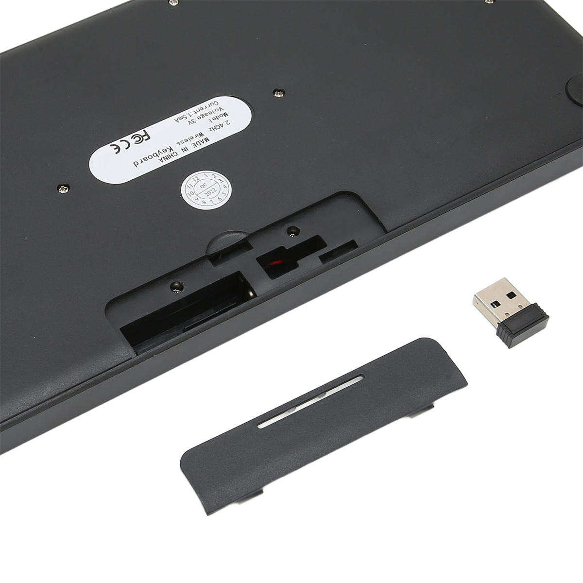 Unterseite einer schwarzen Tastatur mit geöffnetem Batteriefach und USB-Empfänger.