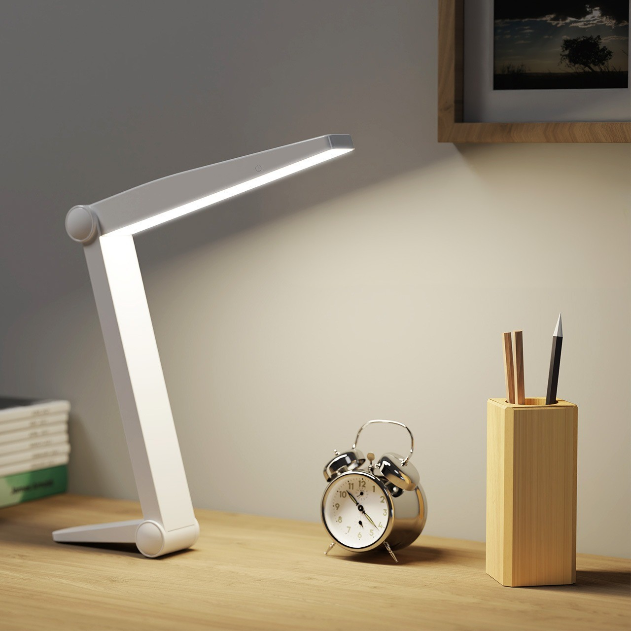 Weiße, faltbare Schreibtischlampe mit Licht, daneben Uhr, Stifthalter und Bücher.