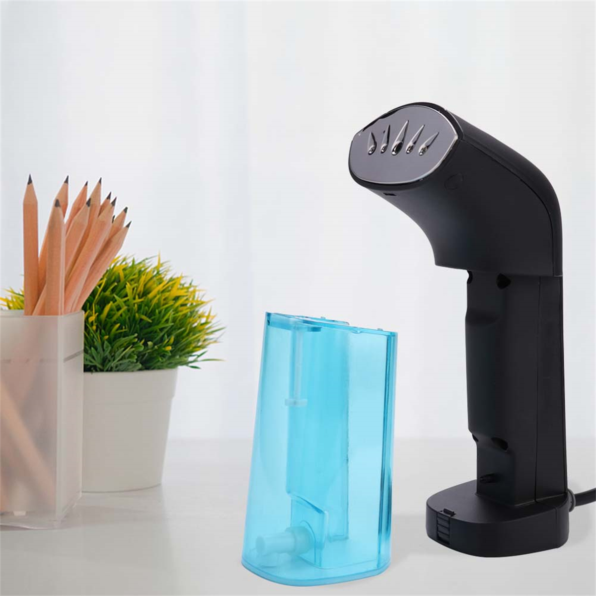 Schwarzer Handdampfer mit blauem Wassertank. Bleistifte in einem transparenten Behälter.