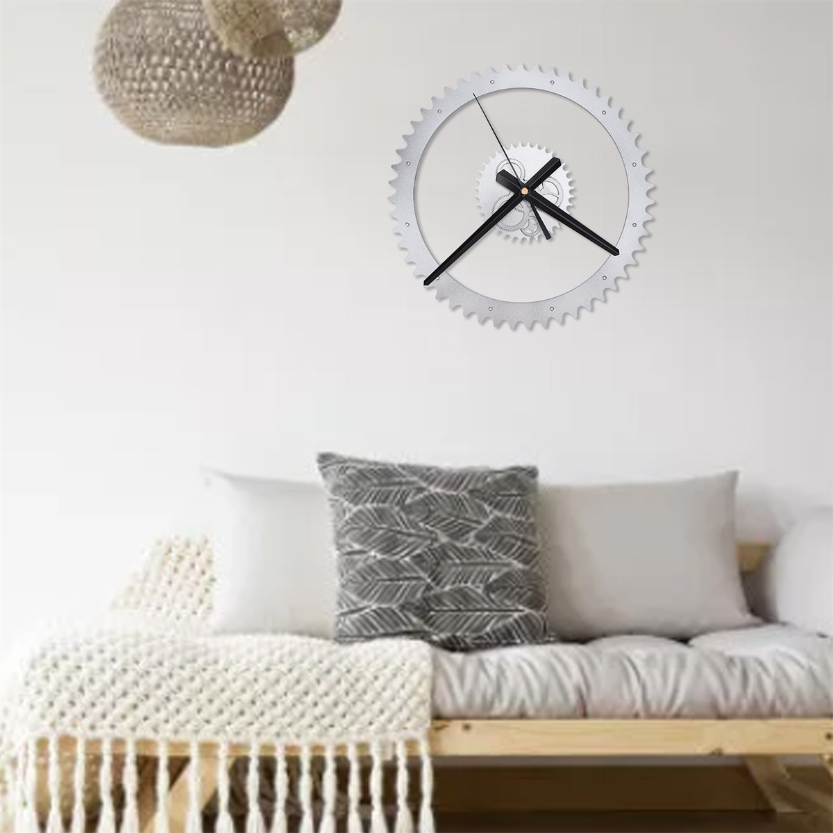 Silberne, zahnradförmige Wanduhr mit schwarzen Zeigern an weißer Wand.