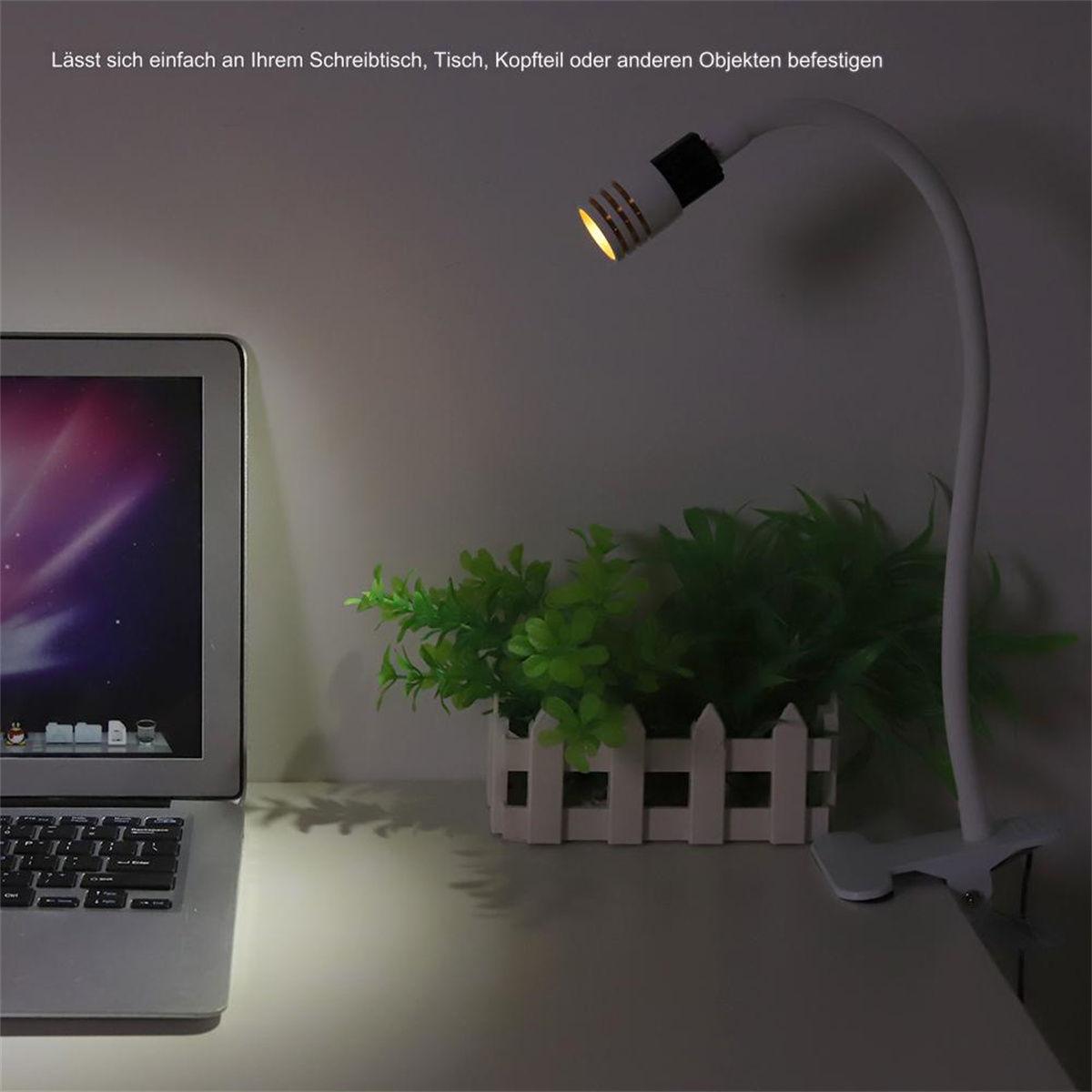 Eine Schreibtischlampe auf einem Schreibtisch neben einem Laptop und einer kleinen Pflanze.