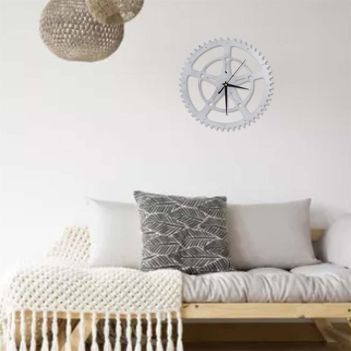 Eine silberne Zahnraduhr hängt an einer weißen Wand über einem Holzbett mit Kissen.