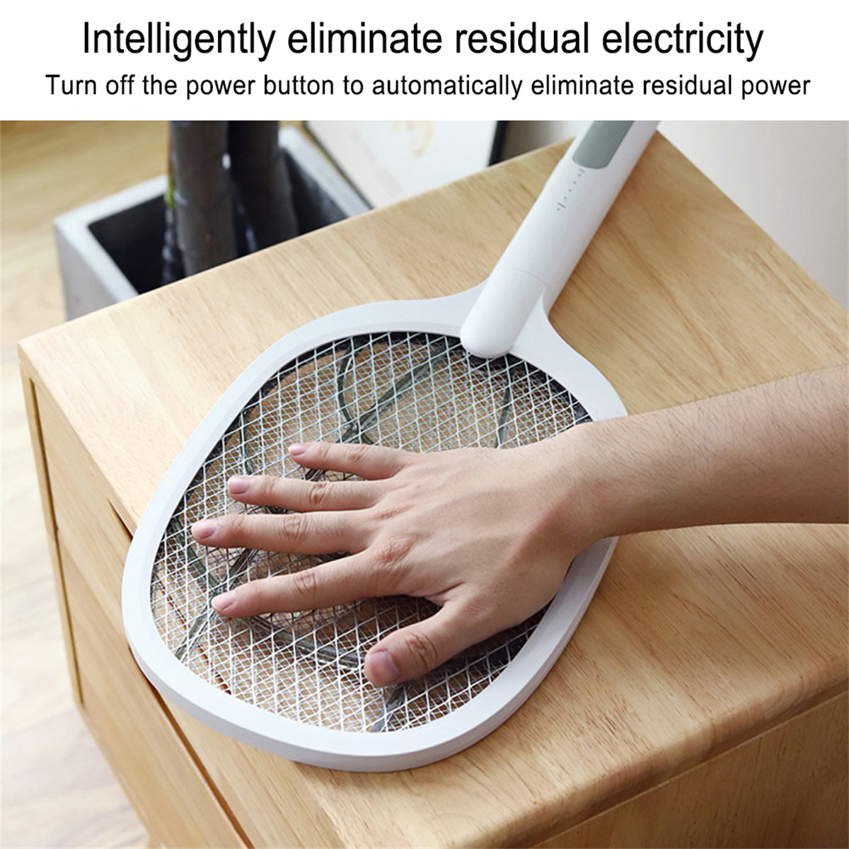 Die Hand einer Person berührt einen weißen elektrischen Fliegenfänger auf einer Holzoberfläche.