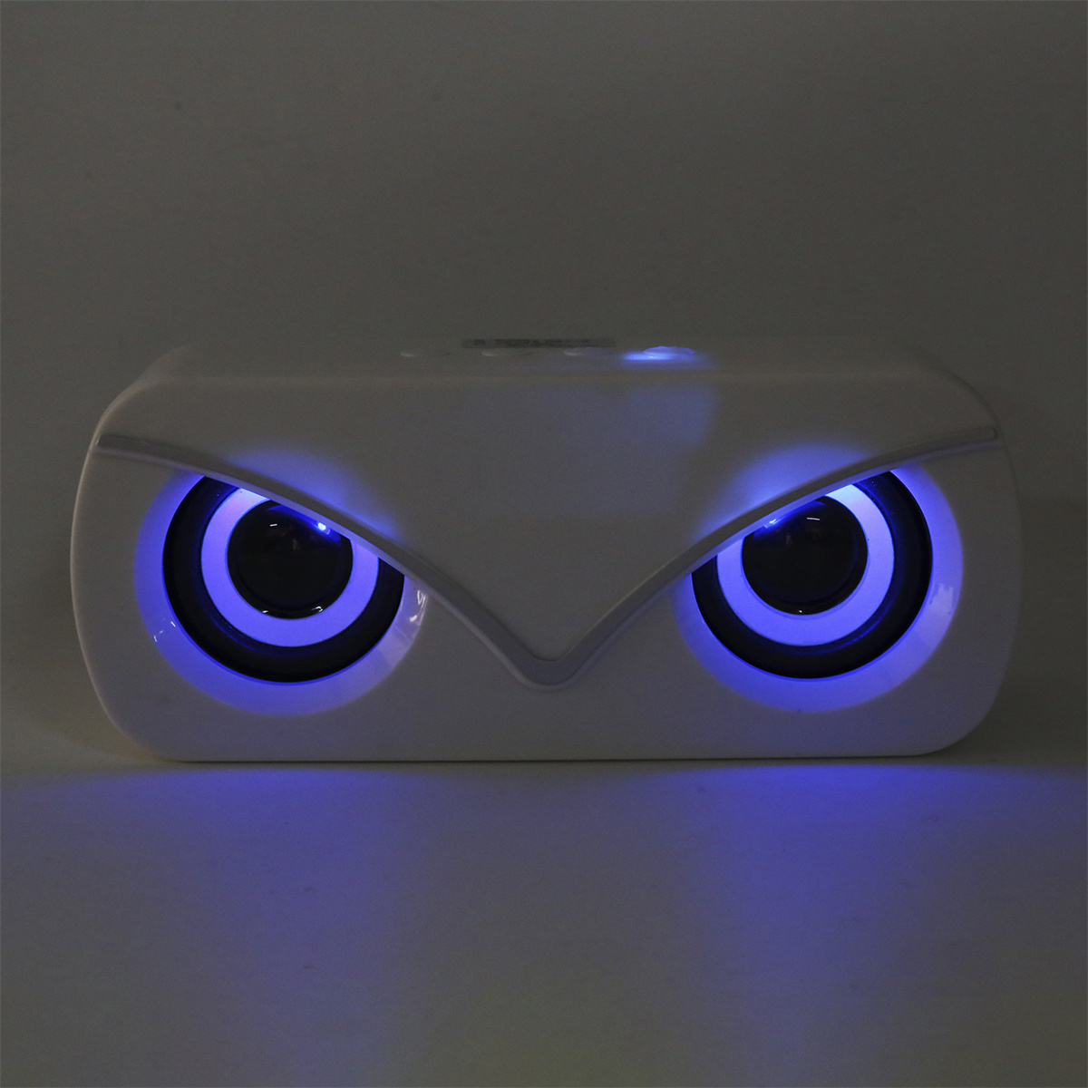 Weißer Lautsprecher mit blauen Augen. Blaues Licht um die Augen. Dunkler Hintergrund, eulenartiges Design.