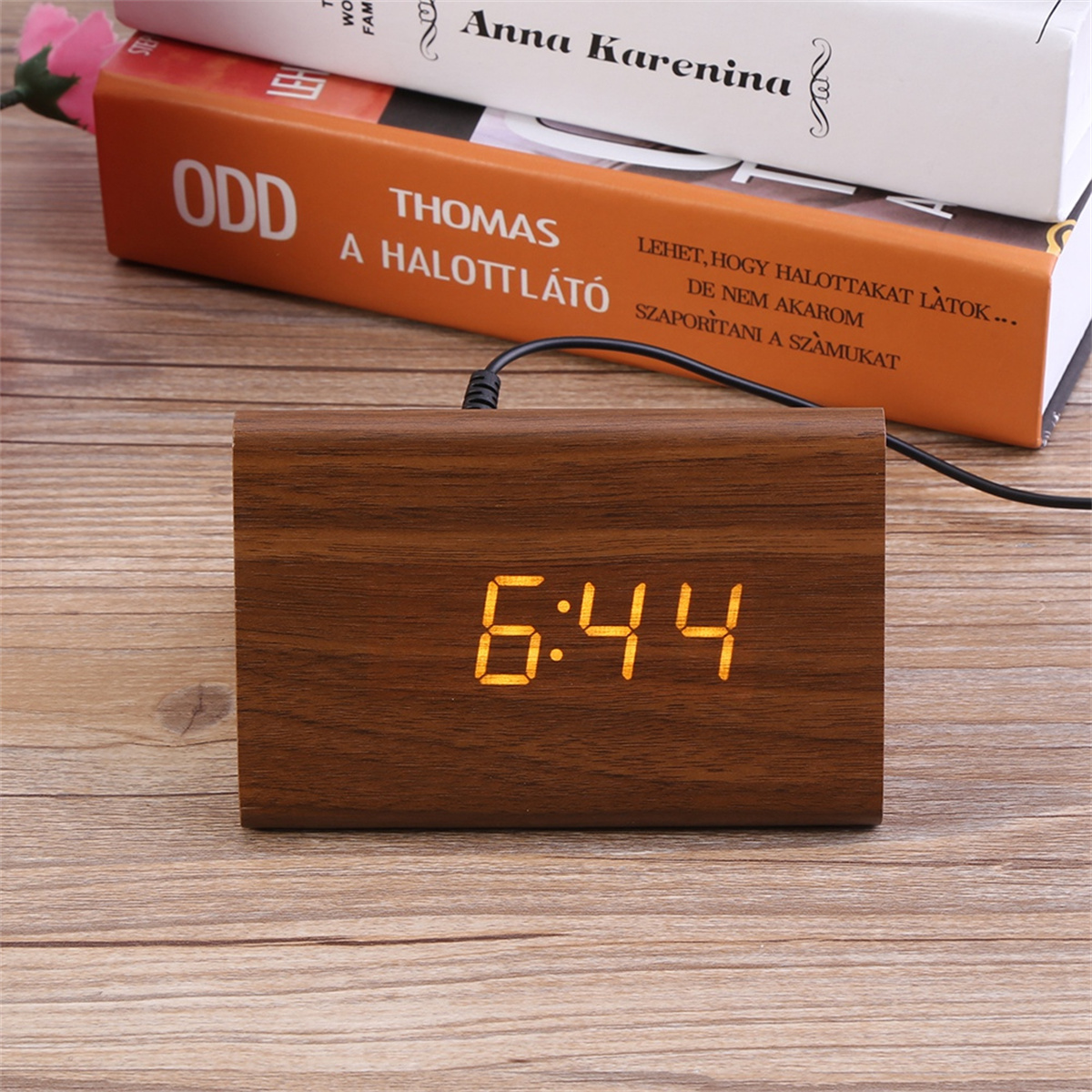 Digitaluhr aus Holz mit der Anzeige 6:44, mit Büchern auf einem Holztisch.
