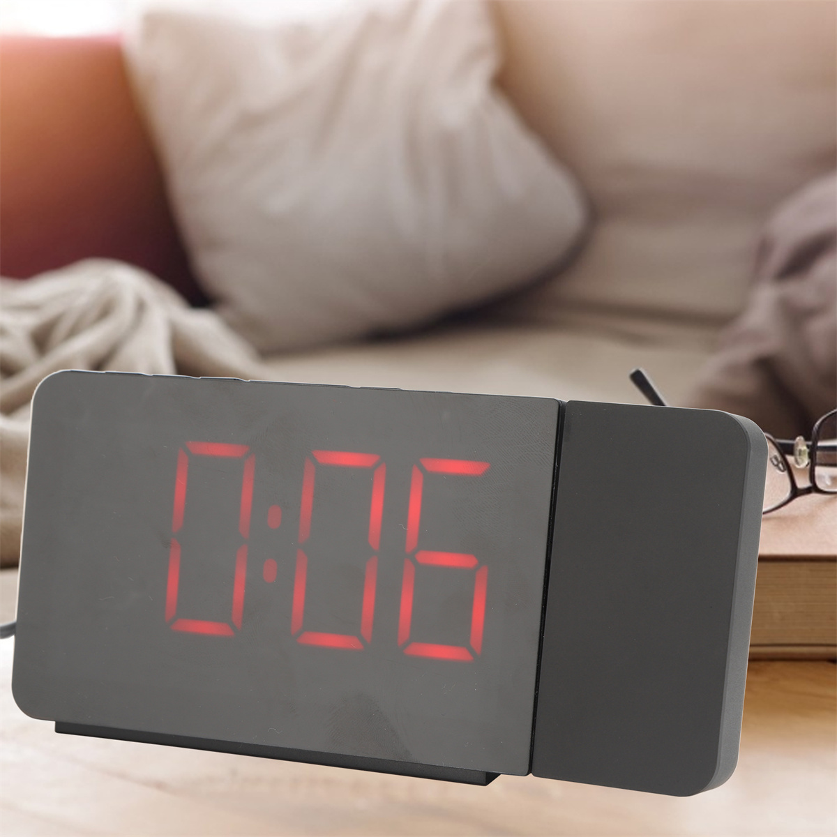 Schwarze Digitaluhr mit der Anzeige 0:06. Rote Ziffern auf schwarzem Untergrund. Ein Bett im unscharfen Hintergrund.