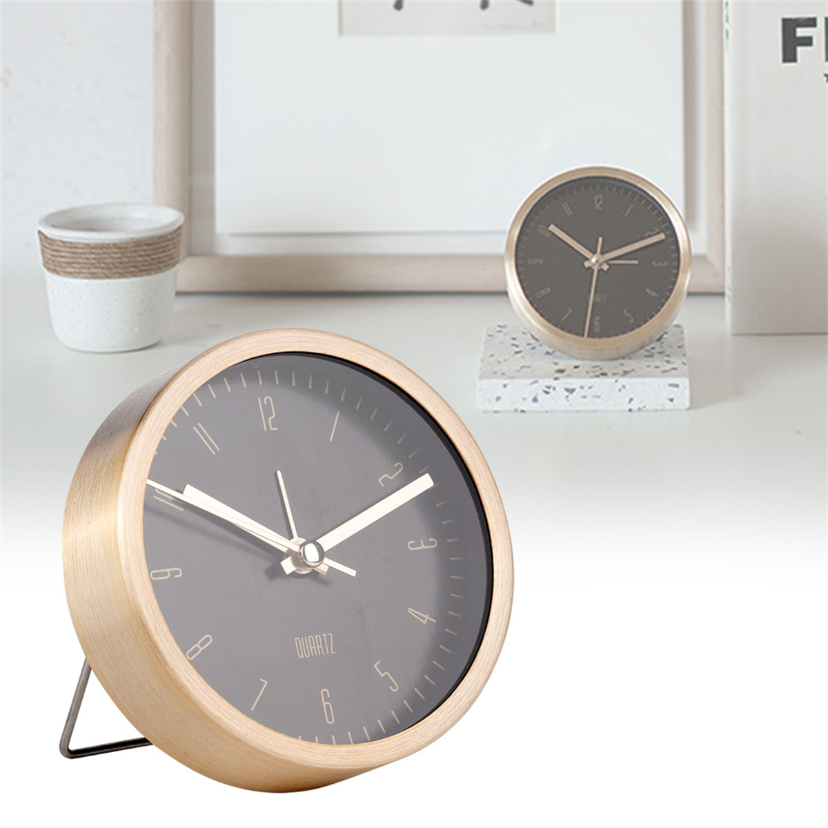 Eine goldfarbene Uhr mit schwarzem Zifferblatt. Eine andere Uhr steht dahinter.