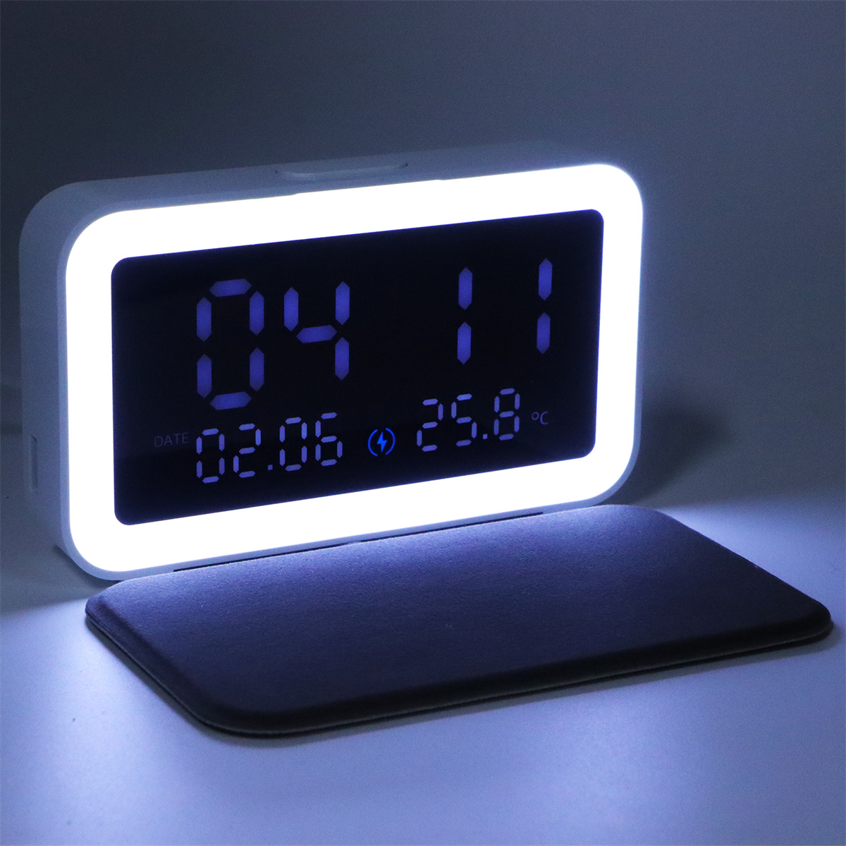 Weiße Digitaluhr mit blau beleuchtetem Bildschirm, zeigt Zeit und Datum.