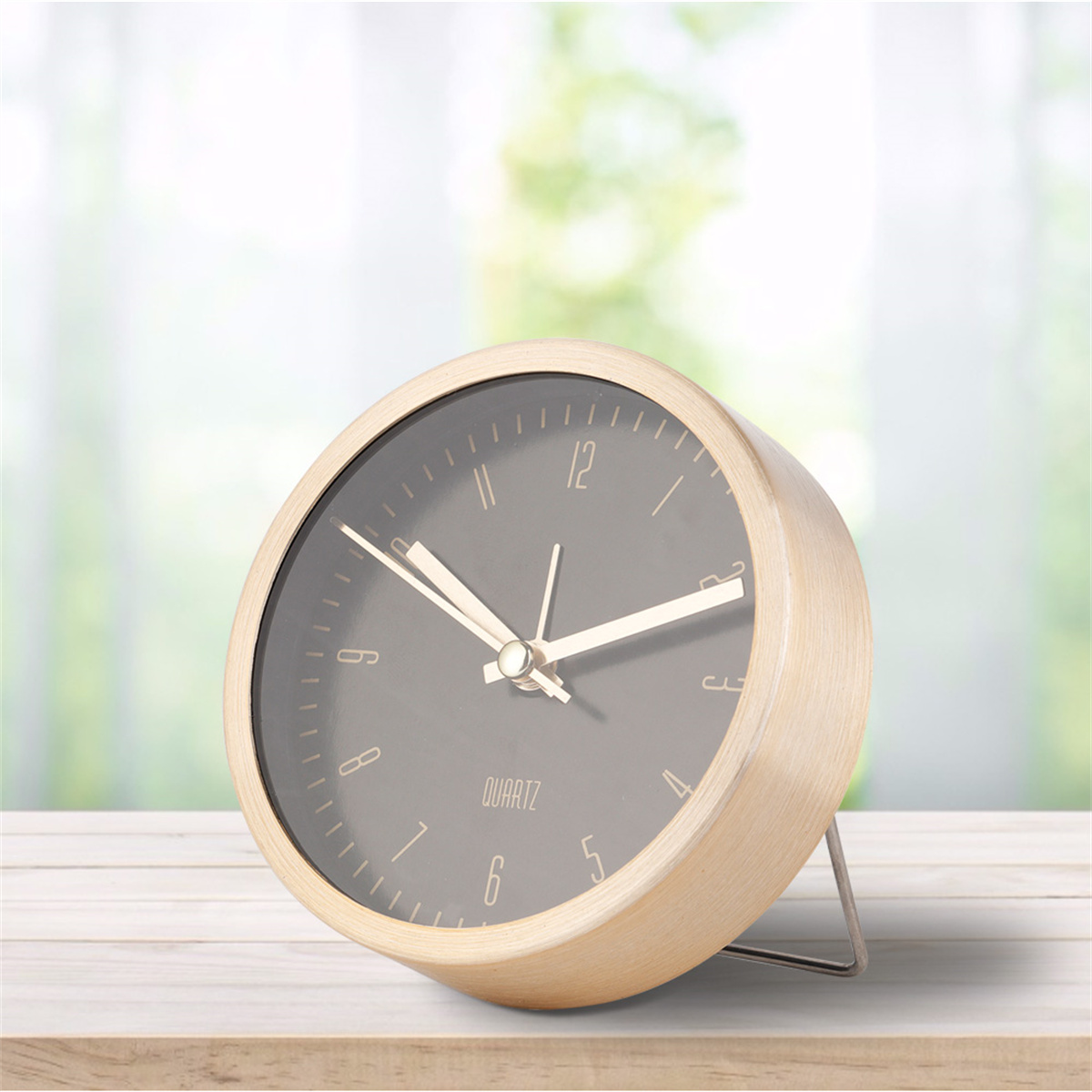 Eine runde Uhr mit goldenem Rahmen, schwarzem Zifferblatt und silbernem Ständer. Auf einem Holztisch.