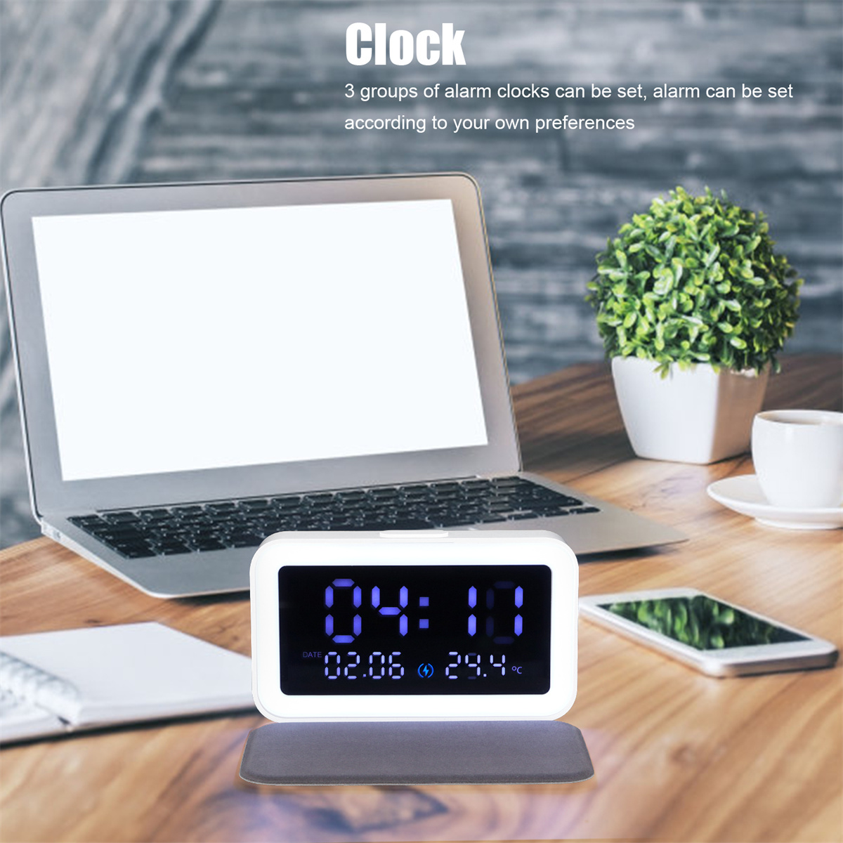 Digitaluhr mit Uhrzeit und Datum, mit Laptop, Pflanze und Telefon auf einem Holztisch.