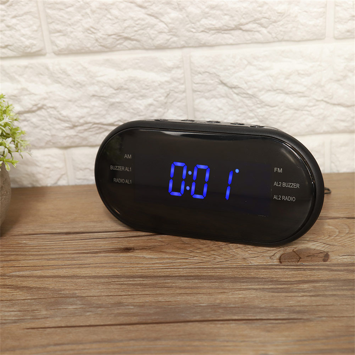 Eine schwarze Digitaluhr, die 0:01 anzeigt. Auf einer Holzoberfläche platziert, mit weißem Ziegelhintergrund.
