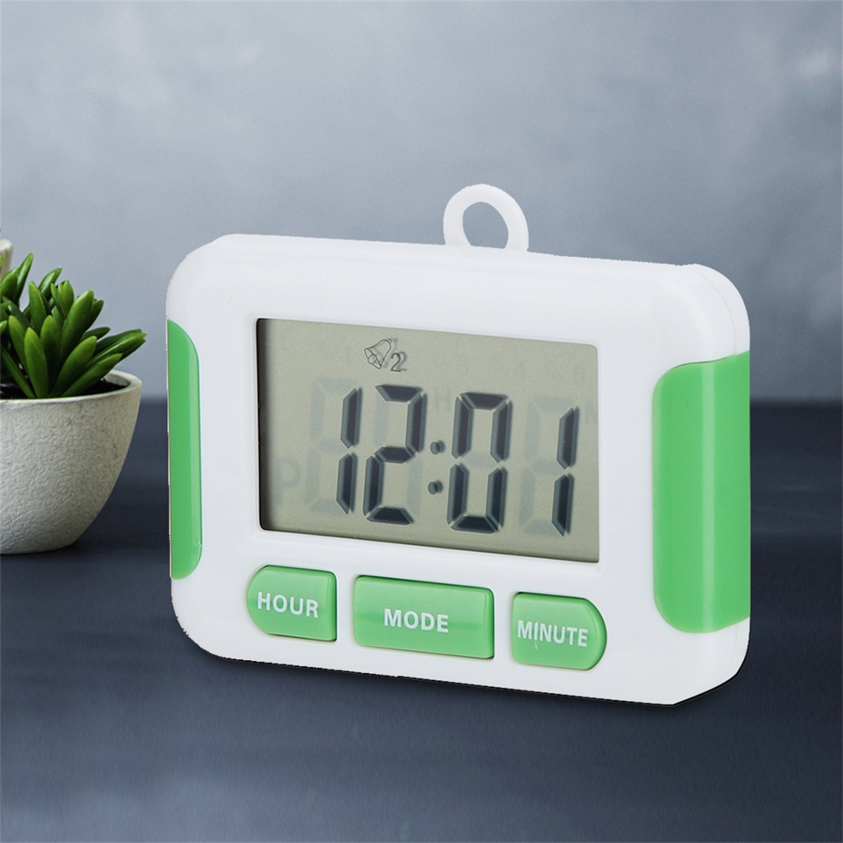 Ein weißer digitaler Timer mit grünen Knöpfen zeigt 12:01 an. Daneben steht eine kleine Pflanze.