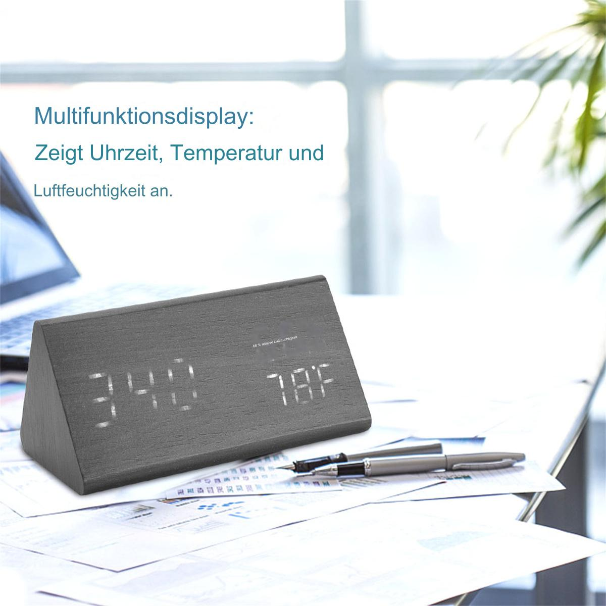 Graue Holzuhr mit Zeit- und Temperaturanzeige, Stifte und Papier auf dem Schreibtisch.
