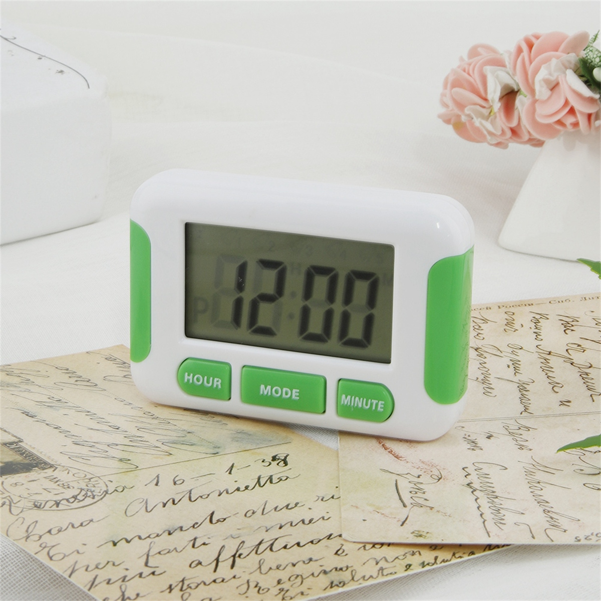 Weiß-grüne digitale Timer-Uhr, die 12:00 anzeigt. Sie hat Stunden-, Modus- und Minutentasten.